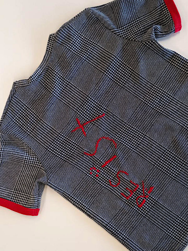 Schwarz-weiß kariertes T-Shirt mit rotem Saum und roter Stickerei 'RESIST' auf der Vorderseite. Black-and-white checkered T-shirt with red trim and red embroidered text 'RESIST' on the front. 