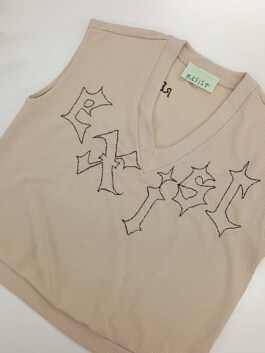 Beiger Strickpullover ohne Ärmel mit V-Ausschnitt und schwarzer, gotisch anmutender Stickerei 'exist' auf der Vorderseite. Am Kragen ein Etikett mit der Aufschrift 'RESIST'. Beige sleeveless knitted sweater with V-neck and black Gothic-style embroidery on the front spelling 'exist'. Label at the collar reads 'resist'. 
