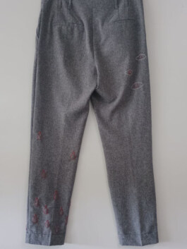 Graue Hose mit Taschen, verziert mit roten, tropfenförmigen Mustern an Bein und Gesäßbereich. Gray pants with pockets, decorated with red teardrop-shaped patterns on leg and seat area. 
