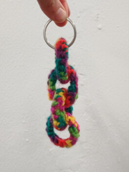 Hand hält einen Schlüsselring mit drei bunten, gehäkelten Ringen aus Wolle. Hand holding a key ring with three colorful crocheted wool rings. 