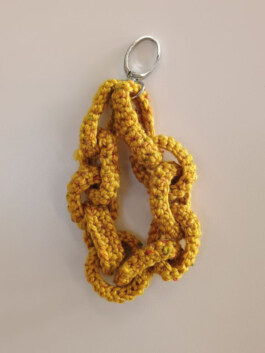 Gelb gestrickte Kette mit großen Gliedern und silbernem Schlüsselring an einem Ende. Yellow knitted chain with large links and a silver keyring at one end. 