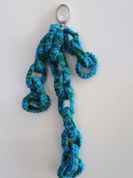 Gehäkelte Kette in Blau- und Grüntönen mit großen, offenen Gliedern, befestigt an einem silbernen Schlüsselring. Crocheted chain in blue and green tones with large open links, attached to a silver key ring. 