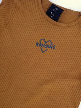 Nahaufnahme eines braunen, gerippten Langarmshirts mit einem blauen Herz und dem Schriftzug 'KONSENS' auf der Brust Close-up of a brown ribbed long-sleeve shirt with a blue heart and the word 'KONSENS' on the chest 