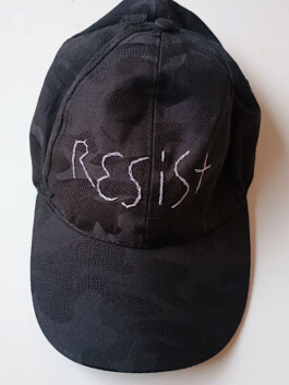 Schwarze Baseballkappe mit Camouflage-Muster und weißer Stickerei mit dem Schriftzug 'Resist' Black baseball cap with camouflage pattern and white embroidered text reading 'Resist' 