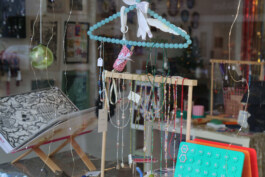 Shop window showing hanging jewelry on a round holder made of blue beads and other items in the background. Schaufenster mit hängenden Schmuckstücken an einem runden Halter aus blauen Perlen und weiteren Gegenständen im Hintergrund. 