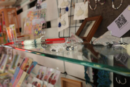 Glass display case with jewelry including bracelets and small figurines with cards and more jewelry on a wall in the background Glasvitrine mit Schmuckstücken, darunter Armbänder und kleine Figuren, im Hintergrund Karten und weitere Schmuckstücke an einer Wand 