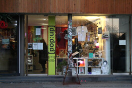 Storefront with various displayed items and a pole covered in stickers in front Schaufenster eines Ladens mit verschiedenen ausgestellten Gegenständen und einem mit Aufklebern beklebten Pfosten davor 