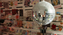 Disco ball hanging in front of a shelf filled with various colorful items and art pieces. Spiegelkugel hängt vor einem Regal mit verschiedenen bunten Gegenständen 
