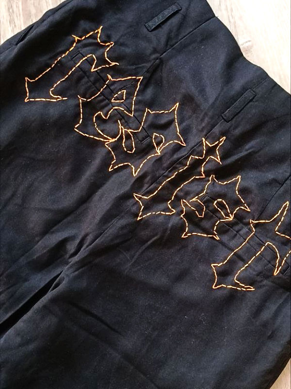Schwarze Hose mit oranger Stickerei in gotischer Schrift, die das Wort 'resist' bildet