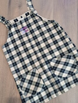 Kariertes Latzkleid mit zwei aufgesetzten Taschen und verstellbaren Trägern auf Holzboden