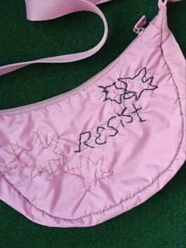 Halbmondförmige, rosa Tasche mit Stickereien in Form von Sternen und dem Schriftzug 'RESIST' 